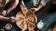 lifestyle image of people reaching for slices of a pizza in a bar setting