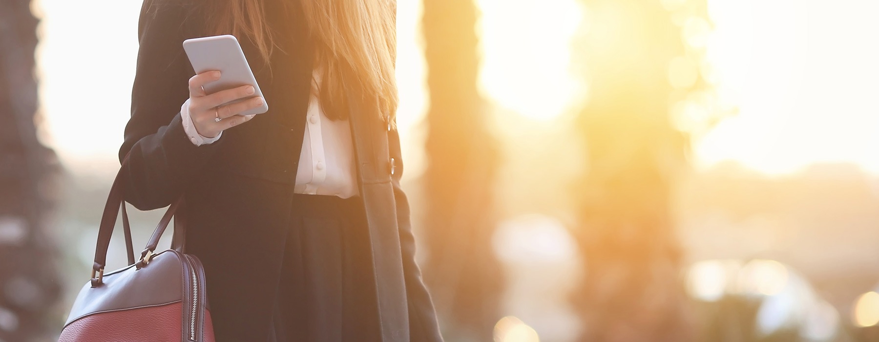 lifestyle image of a woman walking outside at sunset with her phone and purse